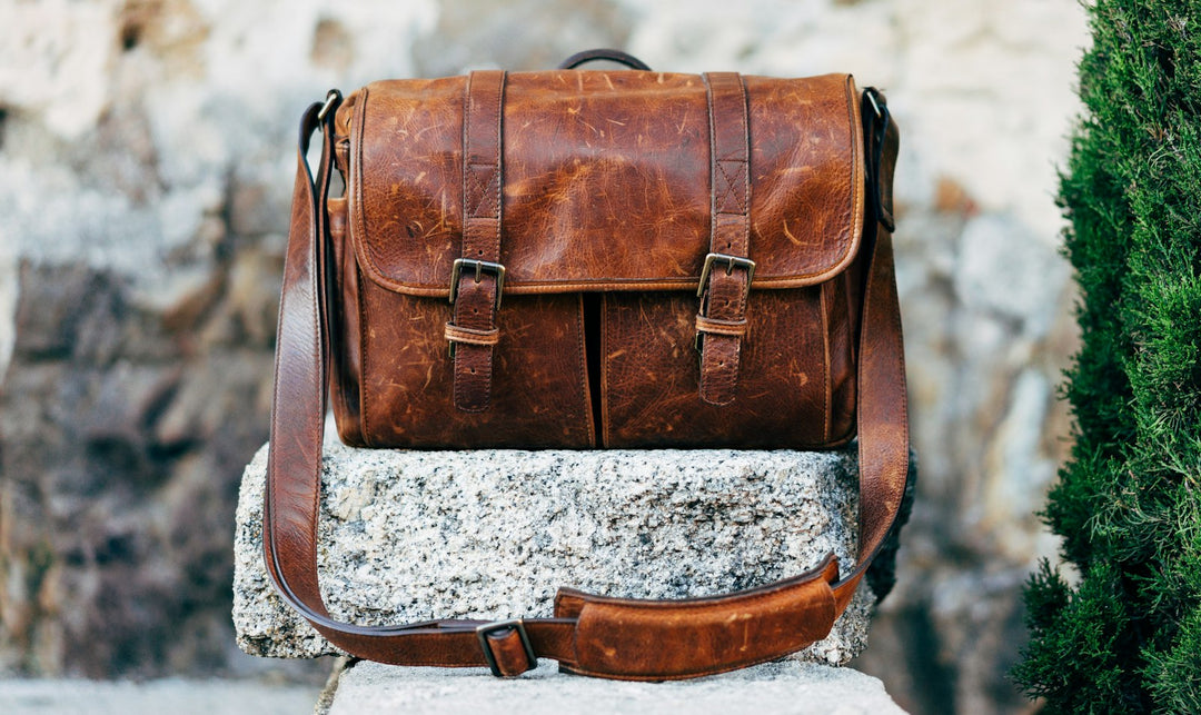 Braune Ledertasche auf grauem Beton neben einer grünen Pflanze